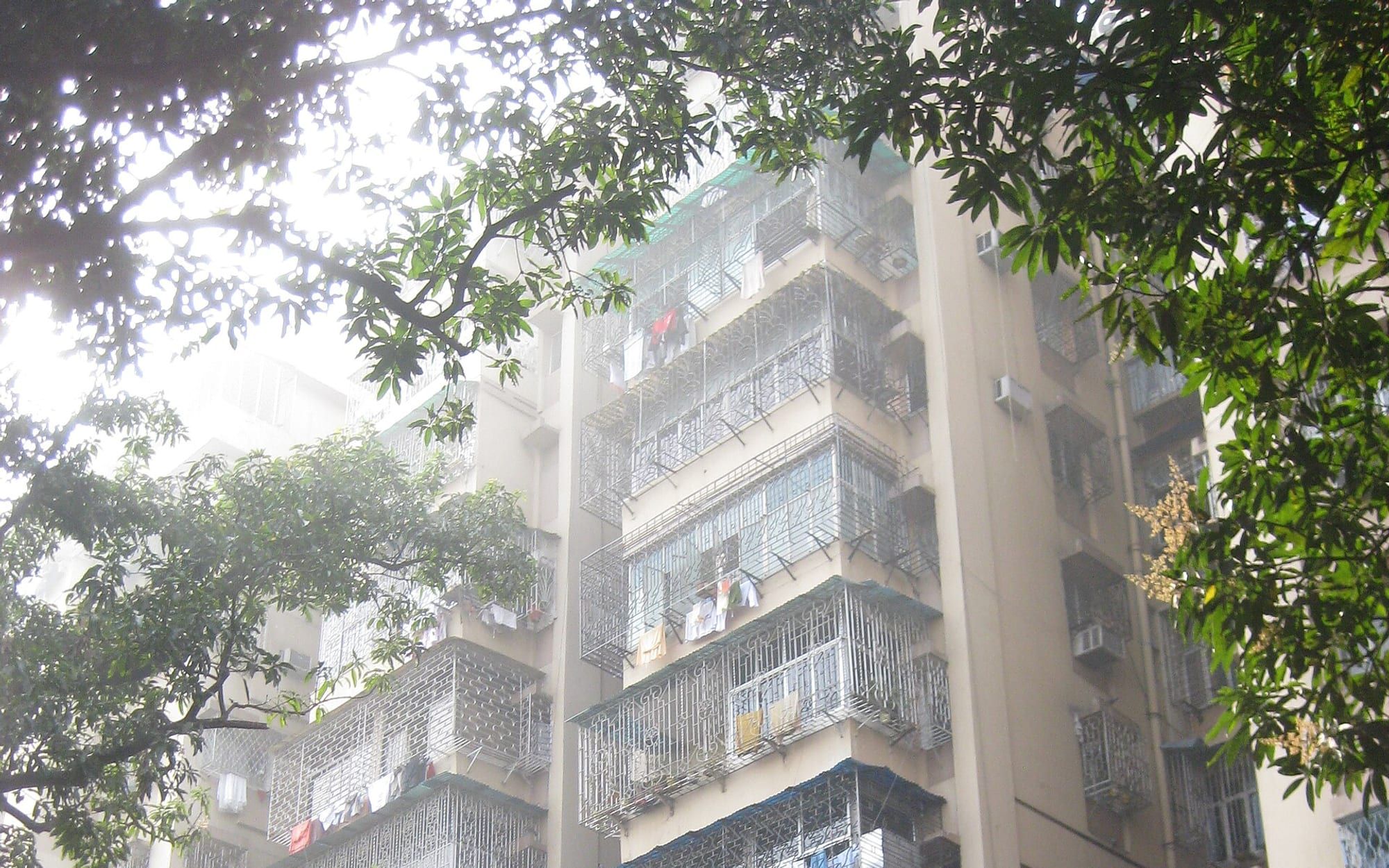 A four-storey residential building in South Kolkata, balconies projecting over a tree-lined street. Stand-in photograph.