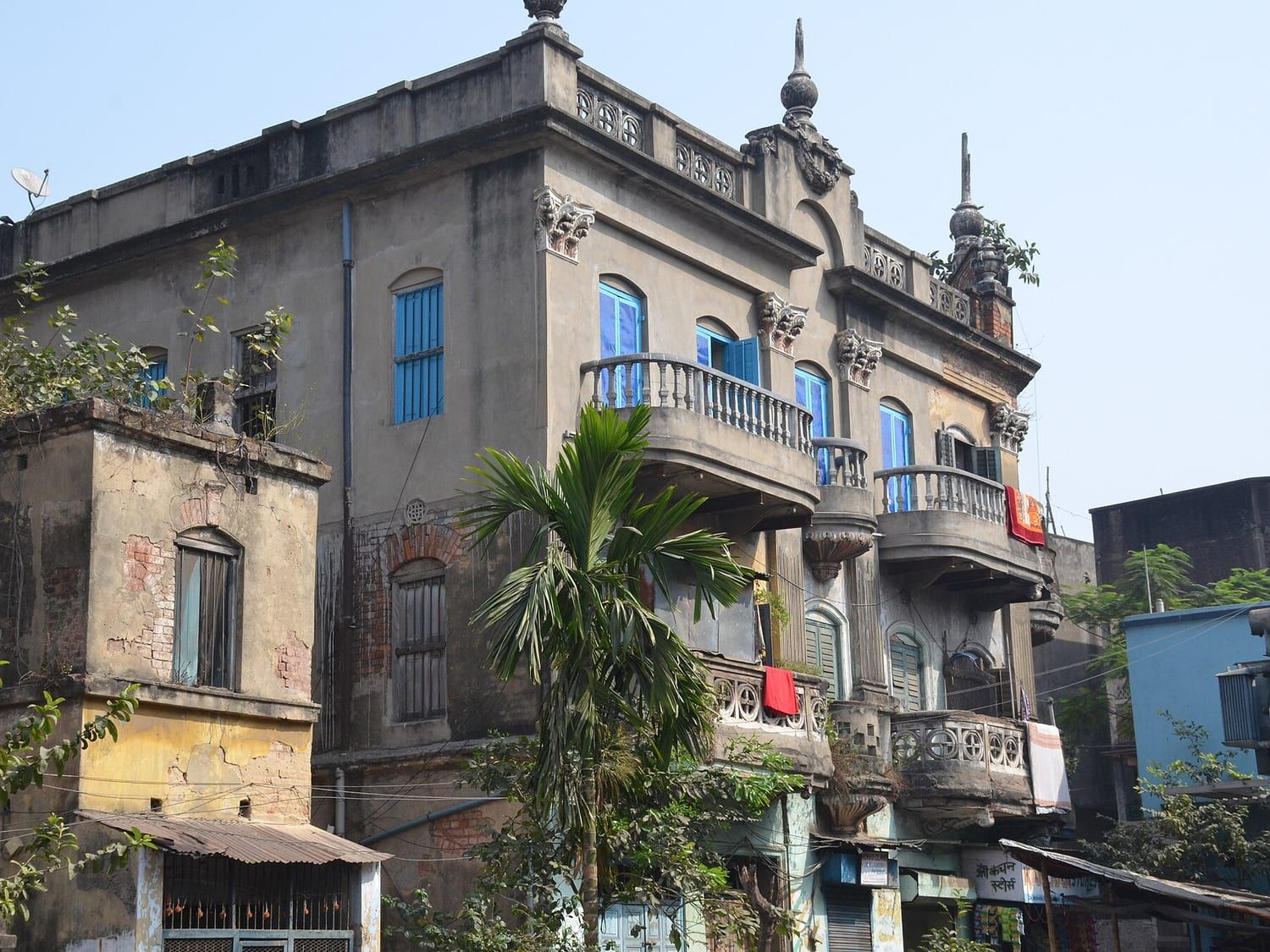 An older Kolkata house with a moulded balcony and shuttered windows on a leafy street. Stand-in photograph.