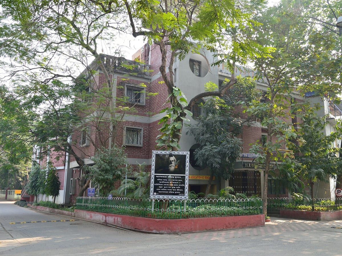 Low-rise apartment building set back behind trees on a quiet residential street. Stand-in photograph for Piyali in Haltu.