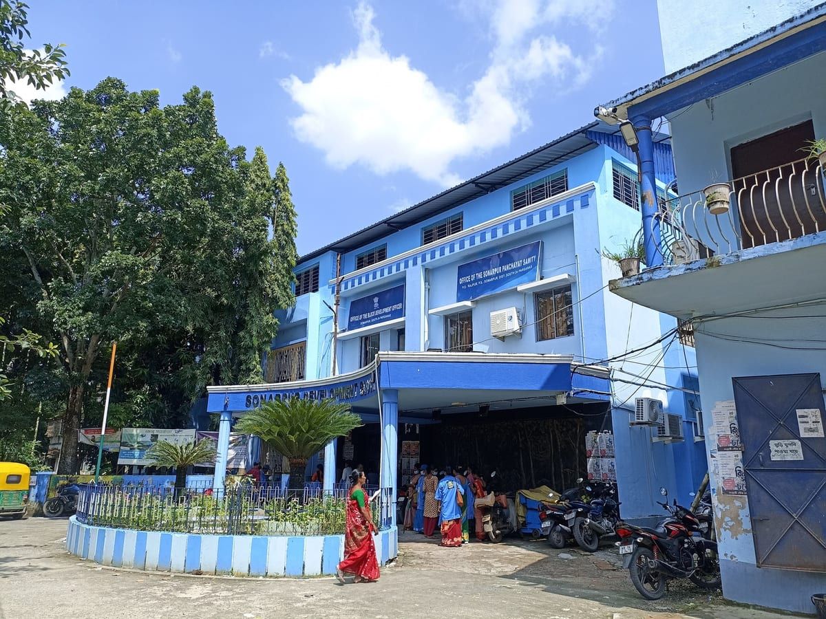 Blue-painted low-rise building at a road junction with a boundary wall. Stand-in photograph for Sanchita in Garfa.