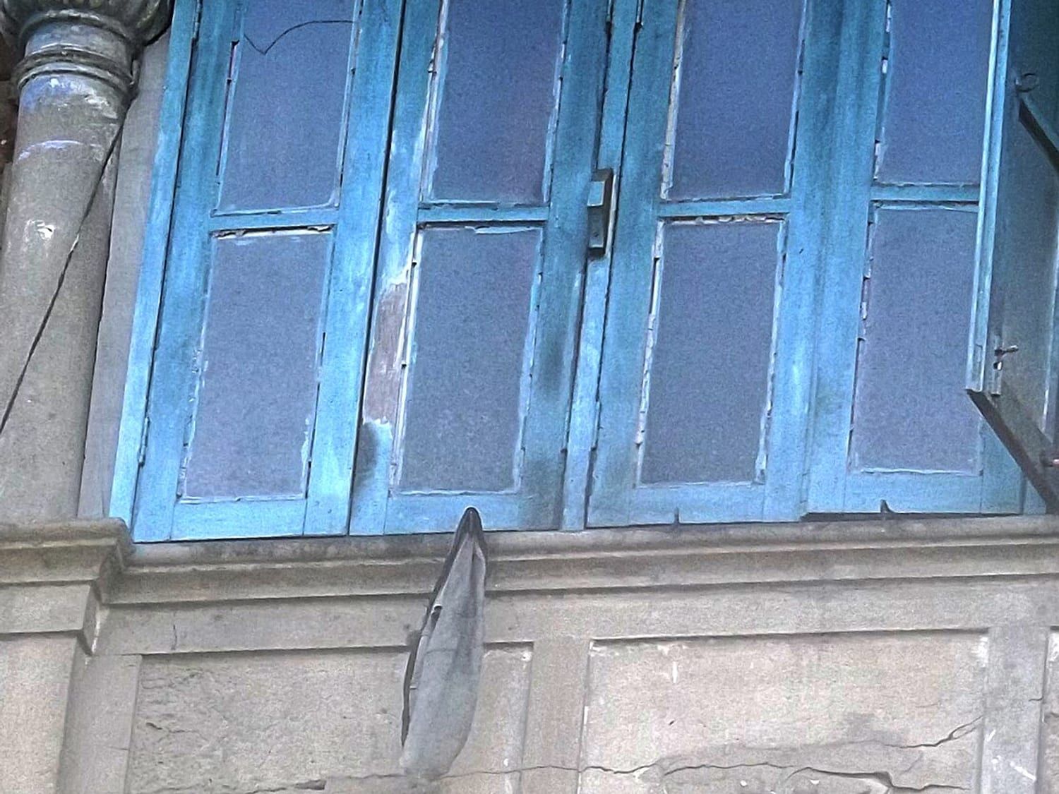 Blue timber louvred window shutters above a moulded plaster panel on an older Kolkata house. Stand-in photograph.